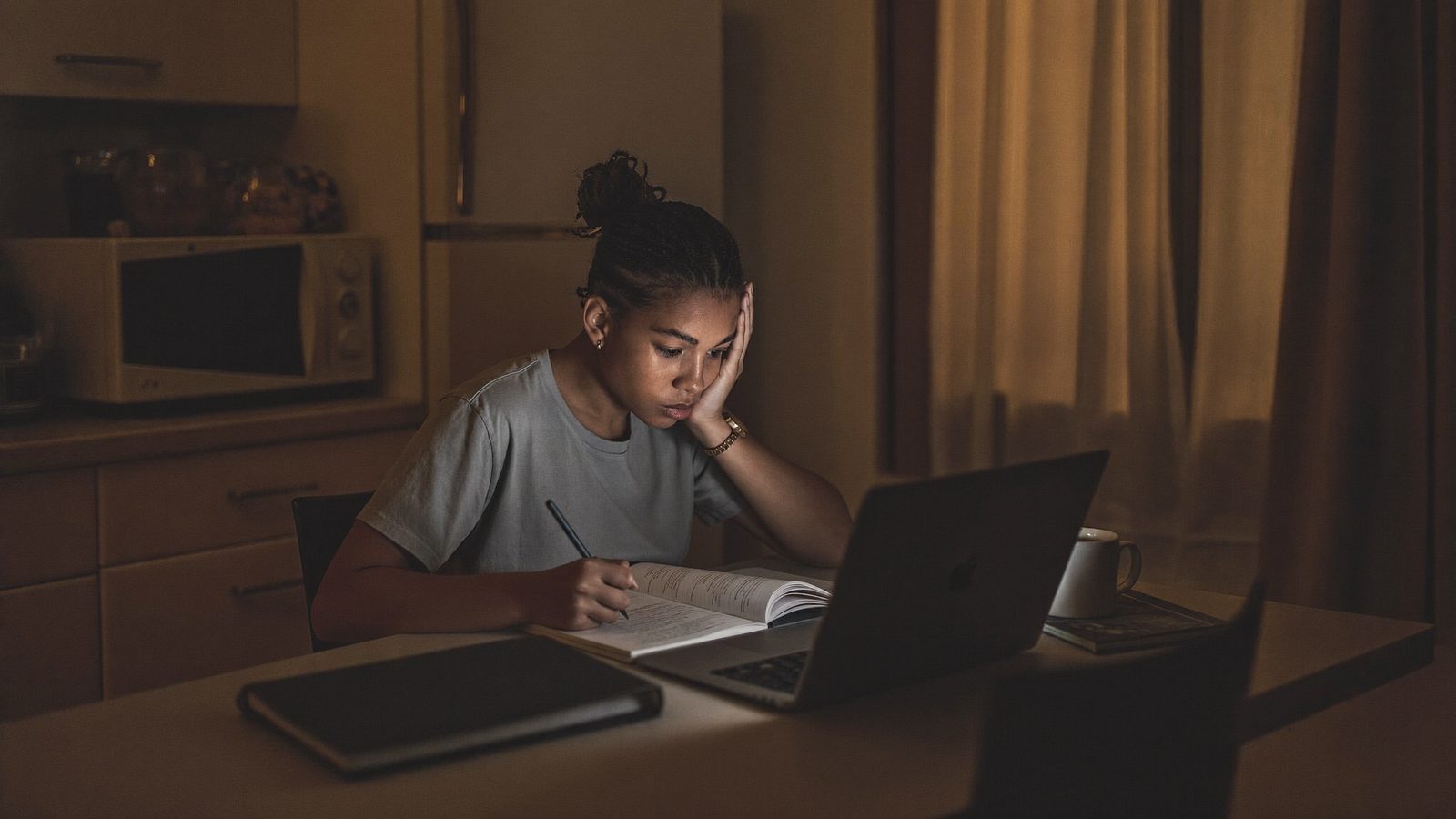 Aluno estudando à noite em casa, no notebook, sob luz baixa